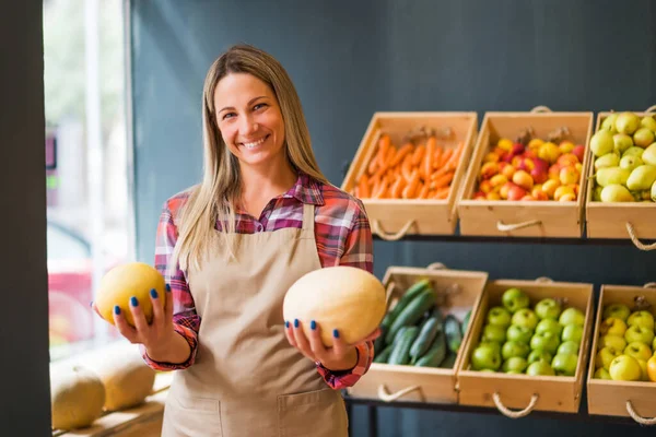 Woman works in fruits and vegetables shop. She is holding melon.