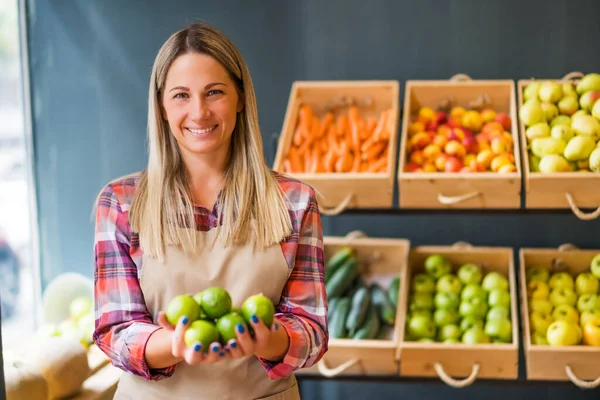 Woman works in fruits and vegetables shop. She is holding lime fruit.