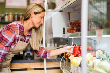 Woman works in fruits and vegetables shop. She is examining goods.