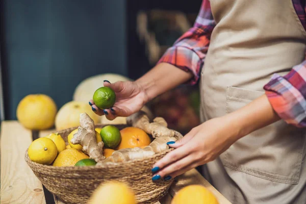 Woman works in fruits and vegetables shop. She is stacking goods in storefront.