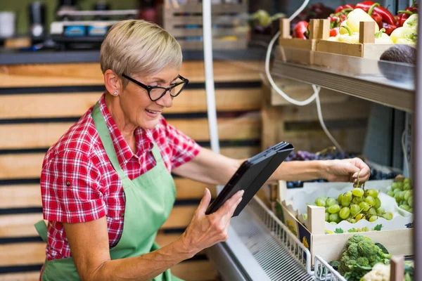 Woman works in fruits and vegetables shop. She is examining grapes.