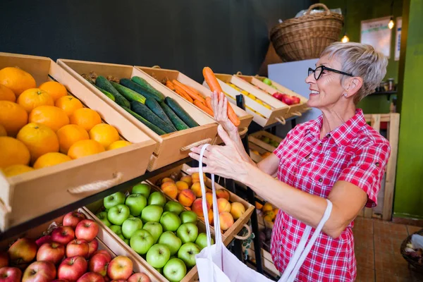 Mature woman buying goods in fruits and vegetables shop.