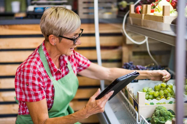 Woman works in fruits and vegetables shop. She is examining grapes.