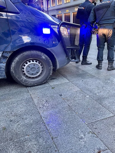 Two national police officers patrolling next to a van with blue lights on in spain.