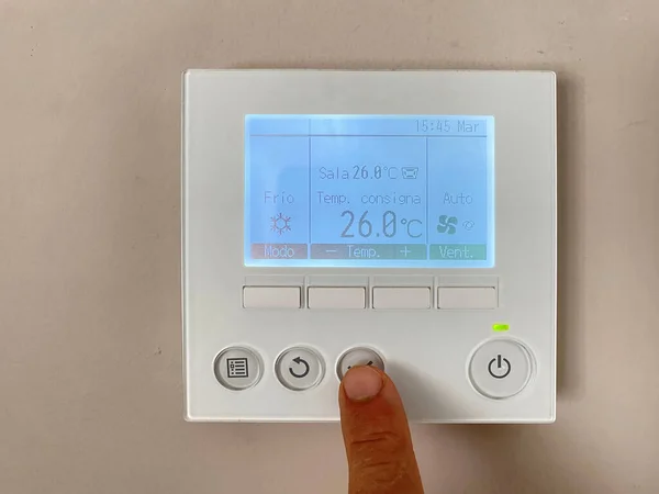 Elektrik faturasında daha az ödeme yapmak için evdeki dijital termostatı ayarlayan elin yakın çekimi.