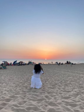 Woman photographing the sunset at the beach with her mobile phone