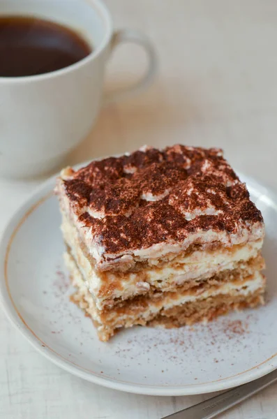 Piece of chocolate cake tiramisu with coffee and cup of tea on white wooden background
