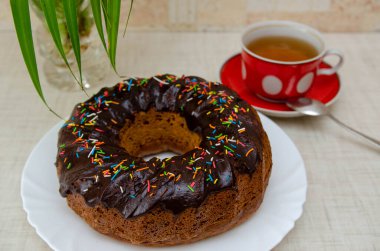 Yuvarlak kek, beyaz tabakta çikolatalı ve kırmızı bardakta.