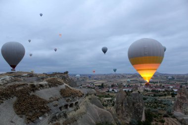 Antik şehir ve kayaların üzerinde gökyüzündeki insanlar için sepetli iki büyük ve bir sürü küçük balon.