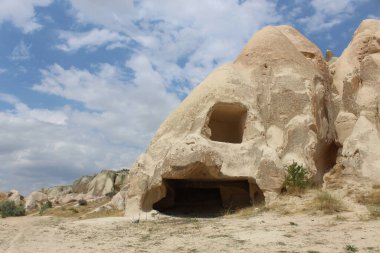 Beyaz bulutlu mavi gökyüzünün altında koni şeklindeki kayaların içinde yapılmış antik konutların kalıntıları.