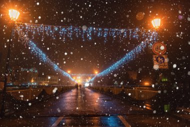 Uzhhorod, Ukraine  January 03, 2022: Night city view of the pedestrian bridge in the center of the town with Christmas and New Year decorations, festive winter cityscape, Zakarpattia