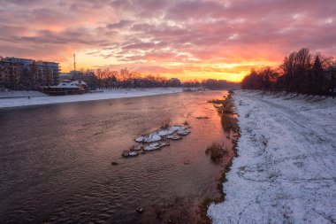 Scenic view of the river Uzh and snowy banks, fiery winter sunset cityscape with colored sky, sun and reflection in the water, outdoor travel background, Uzhhorod, Ukraine