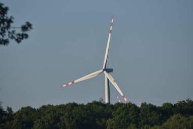 Ormanın arkasından çıkan rüzgar türbini, yaz boyunca şahin.