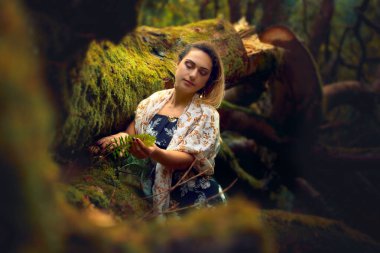 İyi giyimli sarışın kadın, yosunlu bir ağaca dokunuyor.