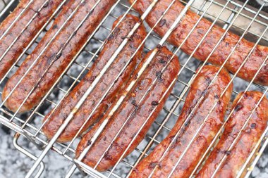 Izgara ızgaralarının arasına sıkıştırılmış et sosisleri ızgarada kızartılıyor. Yakın çekim.