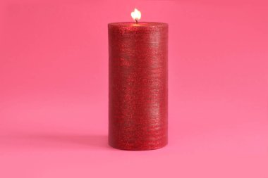 Pembe arka planda yanan kırmızı mum. Yakın çekim.