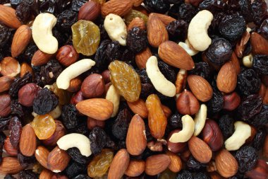 Top view of a pile of large shelled almonds, shelled hazelnuts, cashew nuts, large dark blue raisins and yellow raisins, dried cranberries arranged randomly. Closeup