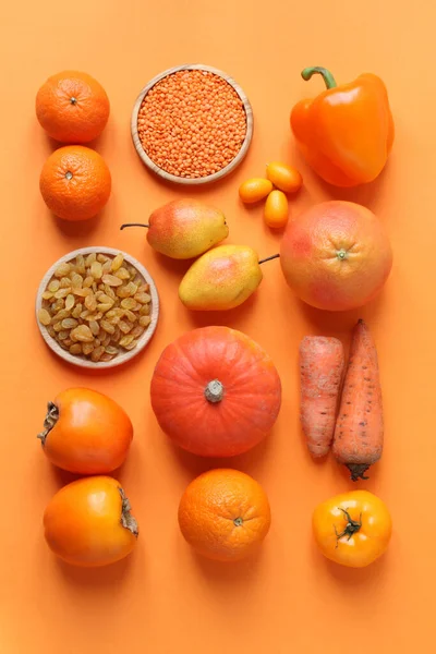 Orange fruits and vegetables on an orange background. Tangerines, pumpkin, persimmons, orange, raisins, pears, dried lentils, grapefruit, kumquat, paprika, carrots, tomato. Top view. Closeup.