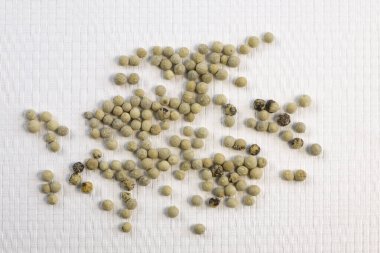 Baharatlar, beyaz biberler, beyaz desenli arka plana serpiştirilmiş biber tohumları, yakın çekim üst görüş dar odak çizgisi, sığ alan derinliği