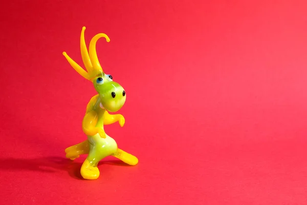 Miniature glass blue yellow dragon figurine isolated on red background