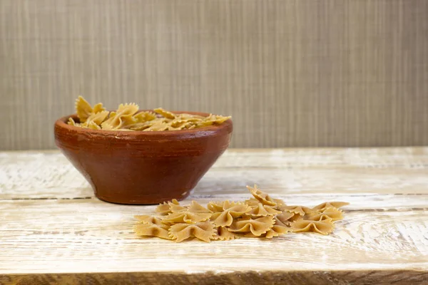 Tam tahıllı, koyu renkli makarna, seçilmiş odaklı, kaba ahşap bir arka planda kahverengi tabakta eğilir.