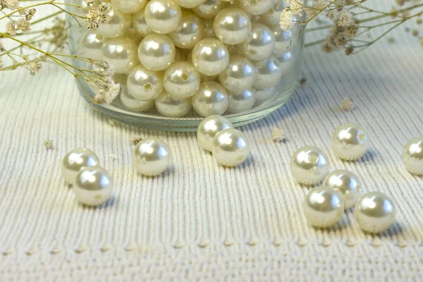 Brillantes perlas blancas hermosas dispersas sobre fondo texturizado de punto blanco, de cerca —  Fotos de Stock
