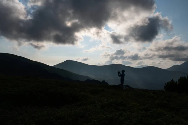 山の上の日没に携帯電話を持っている男の手のシルエット。男性は携帯電話で写真を撮る。太陽の輝きがシルエットを照らす. — ストック写真