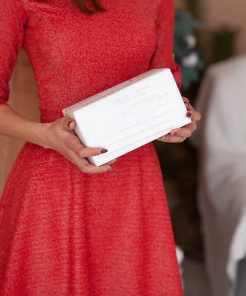 Mujer linda en un vestido, sosteniendo regalos con sus manos, sonriendo, mirando a la cámara sobre un fondo rojo. — Foto de Stock