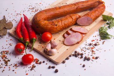 salami sausages from boiled meat on a dark board with pepper, cucumber, tomato, onion and spices. View from above