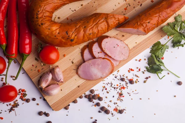 salami sausages from boiled meat on a dark board with pepper, cucumber, tomato, onion and spices. View from above