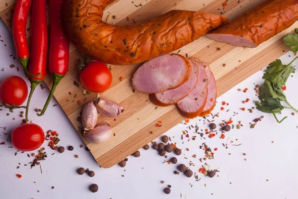 salami sausages from boiled meat on a dark board with pepper, cucumber, tomato, onion and spices. View from above