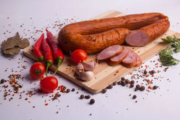 salami sausages from boiled meat on a dark board with pepper, cucumber, tomato, onion and spices. View from above