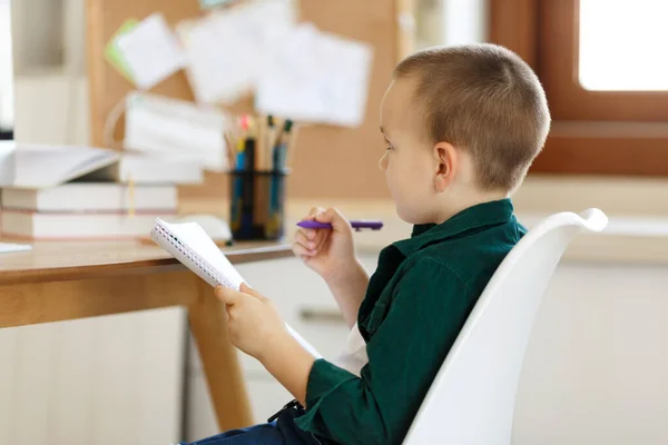 Estudiante de escuela en el escritorio de su habitación. El muchacho usa el portátil y escribe en el cuaderno. Libros y tabletas sobre la mesa. Estudia en casa durante la cuarentena. Pantalla verde —  Fotos de Stock