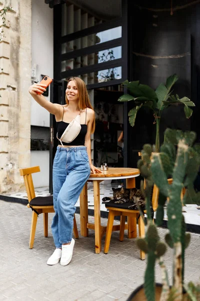 Porträt eines attraktiven, fröhlichen jungen Mädchens mit Smartphone, Blogger macht Selfie oder Live-Übertragung in der Innenstadt im Freien Caféplatz — Stockfoto
