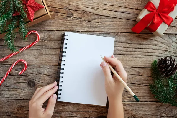 Modèle de Noël avec notebook.Top vue mains de femmes écrivant une wishlist sur une table en bois décorée. . Sapin et décorations festives. Concept Nouvel An — Photo