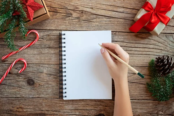 Modèle de Noël avec notebook.Top vue mains de femmes écrivant une wishlist sur une table en bois décorée. . Sapin et décorations festives. Concept Nouvel An — Photo