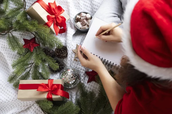 Top vue femme écriture voeux de Noël dans un carnet autour de branches de sapin et cadeaux — Photo