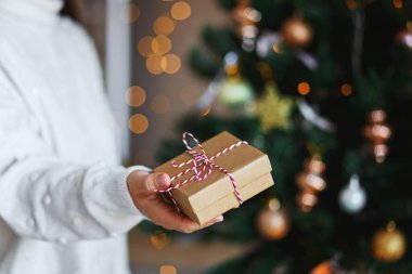 Noel hediyesi, kadınların elinde. Parlayan bokeh, köknar ağacı arka planı. Kış tatili Sıfır atık, plastik yok