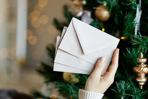 Main tenant pile d'enveloppes en papier artisanal pour la conception d'invitation de carte de vœux de Noël sur fond d'arbre de Noël avec bokeh — Photo