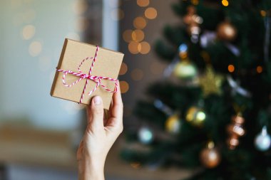 Kadın elinde noel hediyesi. Parlayan bokeh, köknar ağacı arka planı. Kış tatili Sıfır atık, plastik yok
