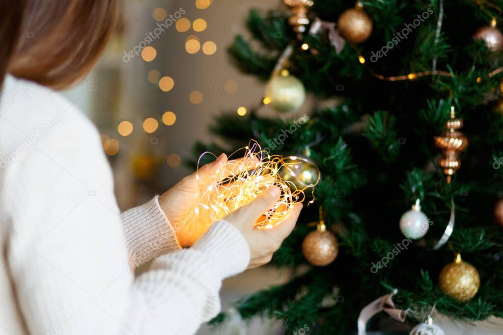 Christmas miracle - woman in white sweater holds glowing led light garland in hands, bokeh background