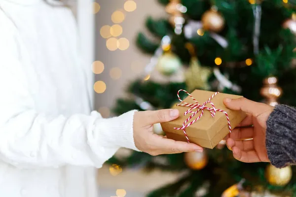 男人把手中的照片和礼品盒剪下来，送给女朋友一份用白色带子系在模糊的圣诞树背景上的礼物 — 图库照片