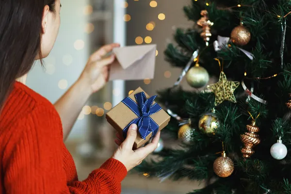 女人在圣诞树旁边打开礼品盒，看贺卡。圣诞时间，新年假期 — 图库照片