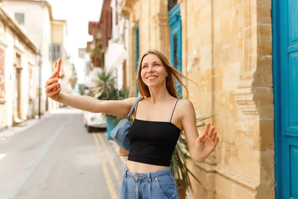 Joven hermosa chica en vaqueros y bolso de mano hace selfie contra el fondo de la ciudad vieja de Chipre — Foto de Stock