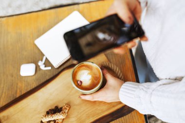 Kadın elleri kahve dükkanında akıllı telefon ve laptopla kahve fincanı fotoğrafı çekiyor.