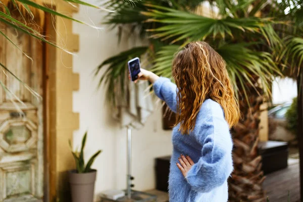 Unerkennbare Frau in blauem Pullover mit brünetten Haaren, die mit dem Smartphone in der Hand streamt und Social-Media-Blogs in modernen Outdoor-Cafés aufzeichnet.Hipster Influencer über soziale Netzwerke — Stockfoto