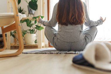 Genç bayan bacak bacak üstüne atmış bir şekilde oturuyor, Sukhasana duruşunda ve meditasyon yapıyor. Evde yoga çalışıyorum. Mutlu genç bir kadın güneşli bir sabah meditasyonunun keyfini çıkarıyor.