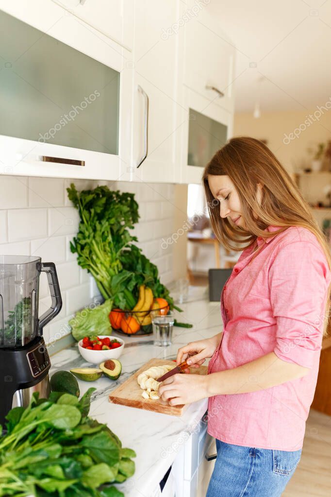 Portrait of beautiful woman chopping fruits smoothies with blender. Healthy eating, dieting lifestyle concept,preparing drink with bananas, avocado and spinach at home in kitchen, mixer on table