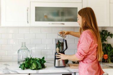 Kadın gülümsüyor, yeşil smoothie 'ye su döküyor. Sağlıklı yiyecekler. Arınma diyetindeki mutlu kadın. Karıştırıcıda doğranmış meyve. 