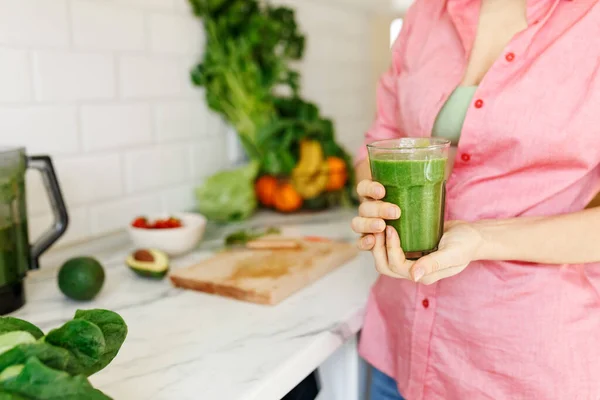 Unrecognizable female holding glass of green spinach detox smoothie